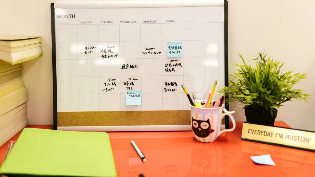 A monthly whiteboard planner on a desk, filled in with meetings and deadlines