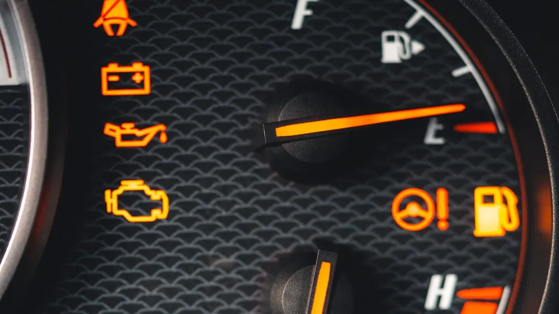 A car dashboard with the seat belt, battery, oil and check engine lights all lit, and the fuel needle resting on empty